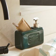 a green soap dispenser sitting on top of a sink next to a towel