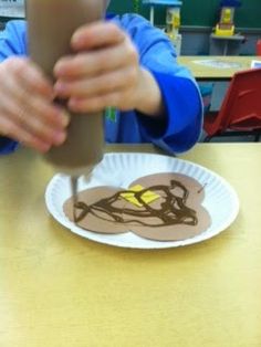 a person holding up a paper plate with chocolate frosting on it in front of a cup