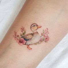 a small duck with flowers on its arm and foot is shown in this tattoo design