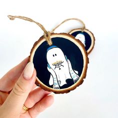 a hand holding a wooden ornament with a ghost on it