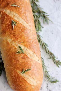 a loaf of bread with rosemary sprigs on it sitting on a marble surface