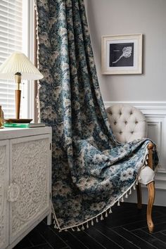 a chair sitting next to a window covered in a blue and white floral print blanket