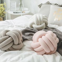 three different colored pillows on a bed with white linens and gray blankets, one is knoted to the side