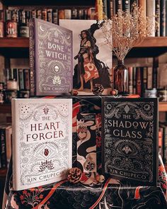 three books sitting on top of a table in front of a book shelf filled with books