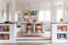 an open living room and dining area with bookshelves on the wall, hardwood flooring and white painted walls