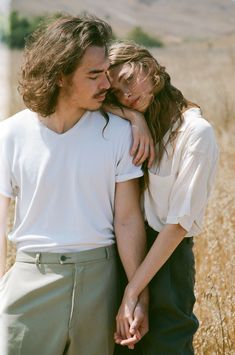 a man and woman standing next to each other in a field with tall grass behind them