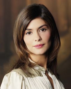 a woman with shoulder length hair standing in front of a painting wearing a white blouse