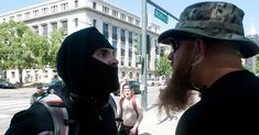 two men in black hoods standing next to each other on the side of a street