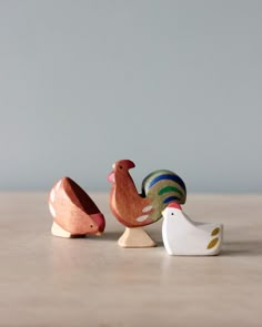 three wooden toy chickens sitting on top of a table next to each other and one chicken standing up