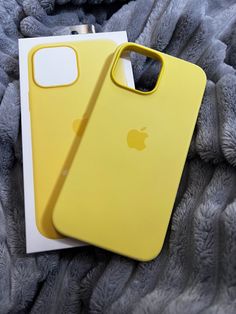 two yellow iphone cases sitting next to each other on top of a gray blanket,