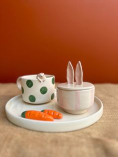 a white plate topped with two carrots next to a cup and saucer on top of a table