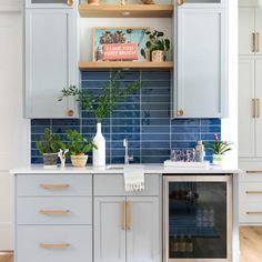 a kitchen with white cabinets and blue tile backsplashing, potted plants on the counter