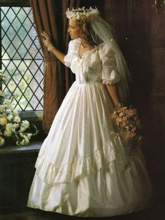 a woman in a wedding dress standing next to a window with flowers on her head