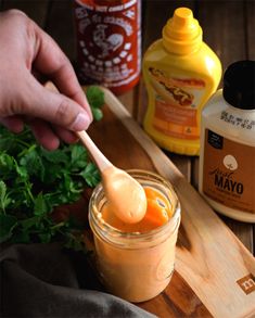 a person holding a wooden spoon over a jar filled with sauce and parsley on a cutting board