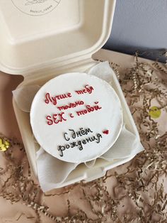 a cake with writing on it sitting in a white box next to some dried flowers