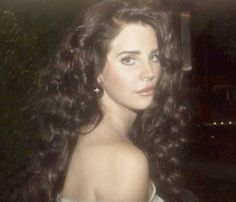 an old photo of a woman with long dark hair wearing a white dress and earrings