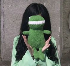 a woman holding a green stuffed frog in front of her face