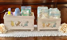 two wooden boxes with baby items in them sitting on a lace doily covered table