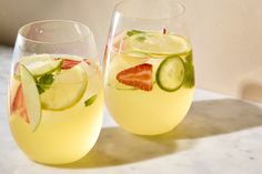 two glasses filled with lemonade, cucumber and strawberries next to each other