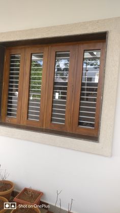 a window with wooden shutters on the side of a wall next to potted plants