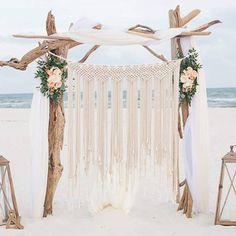 an outdoor wedding ceremony setup with white drapes and flowers on the beach, along with wooden lanterns