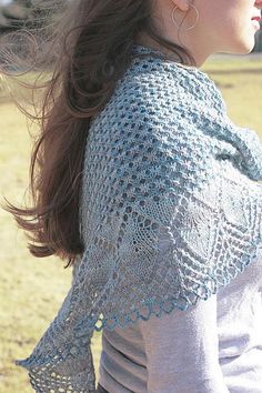 a woman standing in the grass wearing a knitted shawl and earring set