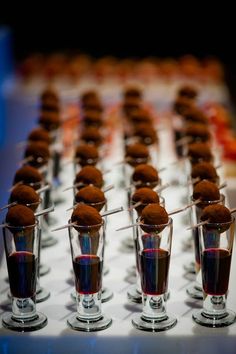 several shot glasses filled with red liquid and chocolate balls on top of each other, lined up in rows