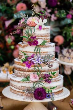 a multi layer cake with flowers on the top is sitting in front of other desserts