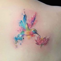 watercolor tattoo on the back of a woman's shoulder with a hummingbird flying over a pink flower