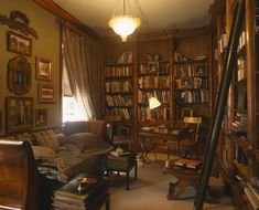 a living room filled with furniture and bookshelves next to a lamp hanging from the ceiling