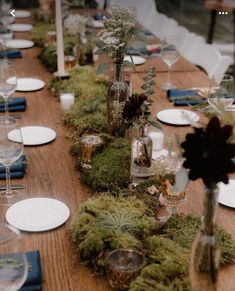 the table is set with white plates and blue napkins, glass vases filled with plants