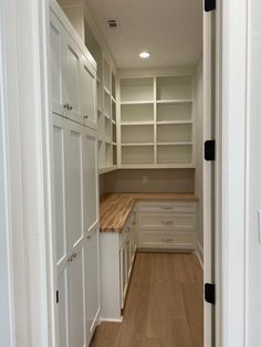 an empty walk - in closet with white cabinets and wooden counter tops, along with hard wood flooring