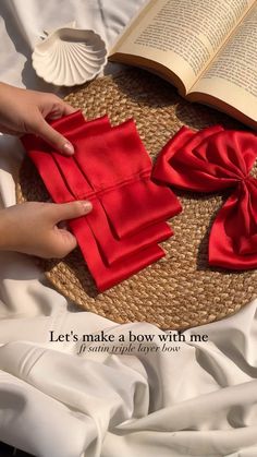 someone is making a bow with red cloth on top of a table next to an open book