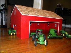 two green tractors are parked in front of a red barn