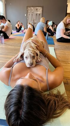 a woman laying on top of a yoga mat holding a dog