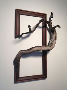 a wooden frame hanging on the wall next to a tree branch with a bird perched on it