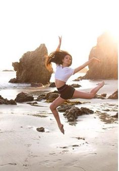 a woman jumping in the air on top of a beach