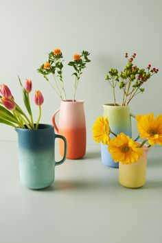 four vases with flowers in them sitting on a white surface, one has yellow and the other is pink