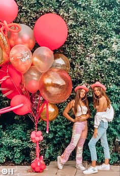 two young women standing next to each other with pink and gold balloons in the air