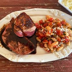 a white plate topped with meat, beans and rice next to a bowl of macaroni salad