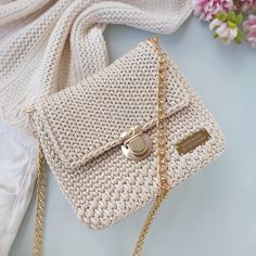 a white crocheted purse sitting on top of a table next to a pink flower