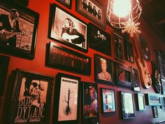 a red wall with many framed pictures on it and a chandelier hanging from the ceiling