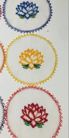 four cross stitch designs in different colors on white paper with red, yellow and blue flowers