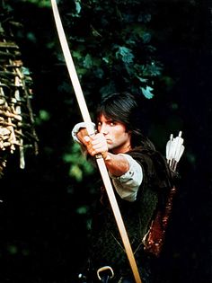 a man dressed in medieval clothing holding a bow and arrow