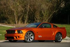 an orange sports car parked on the side of the road in front of some trees