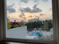 the sun is setting over an empty swimming pool from inside a window with flowers in it