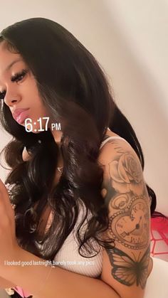 a woman with tattoos on her arm holding a cell phone and looking at the camera