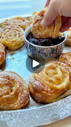 a person dipping some food into a bowl on top of a metal tray with other pastries