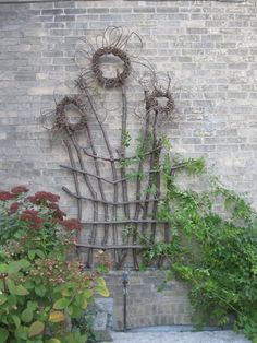 a sculpture made out of branches and vines in front of a brick wall with plants growing on it