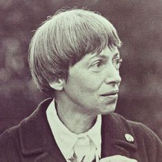 a woman with short hair wearing a suit and tie looking off into the distance while standing in front of trees